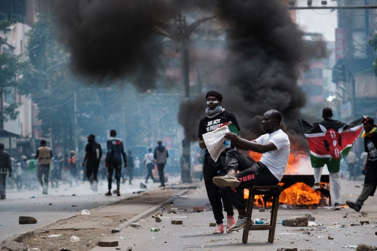A protester holds a newspaper while smoke billows from a burning barricade during an anti-government demonstration in Nairobi.