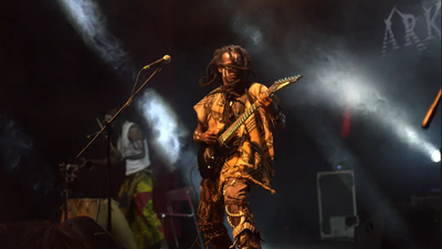 A photo of Rock, the founder and leader of heavy metal band, Arka’n Asrafokor playing the guitar on stage.