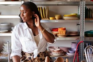 Person in white shirt arranging hair, standing by shelves of colorful dinnerware.