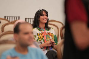 Menna Shanab wearing a green and white jersey, smiling in a conference room full of chairs. 