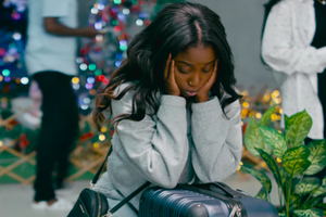 A woman sitting with her head in her hands in front of a Christmas tree. 