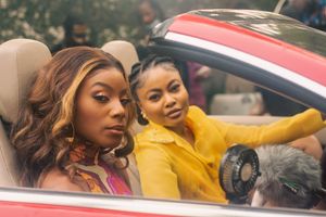 Two women sitting in a red convertible and staring sideways at the camera.